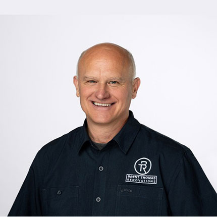 A man with a bald head smiles at the camera, wearing a dark button-up shirt with "Brent Thomas Renovations" logo on it.