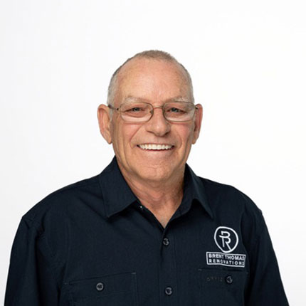 Man wearing glasses and a black button-up shirt with a logo on it smiles against a plain white background.